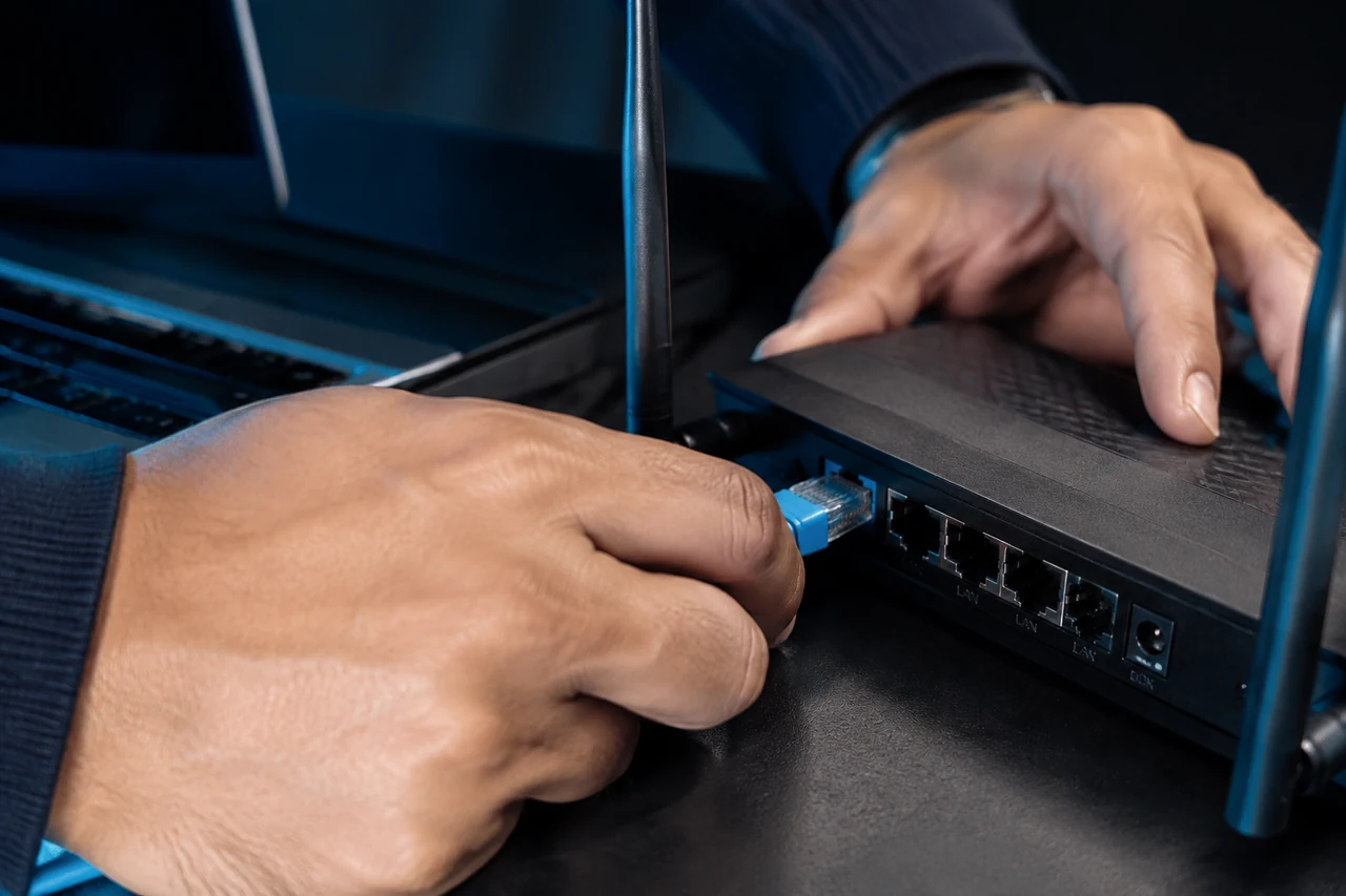 Conexão de cabo de rede em roteador compacto ao lado de um notebook